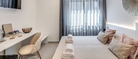 Una habitación de hotel moderna con cama, escritorio, silla, televisor y un ventanal con cortinas.