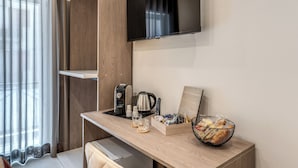 A modern hotel room with a wooden desk, a flat-screen TV, a coffee maker, a kettle, and a basket of snacks. - B&B Welcome Inn Napoli (Naples)