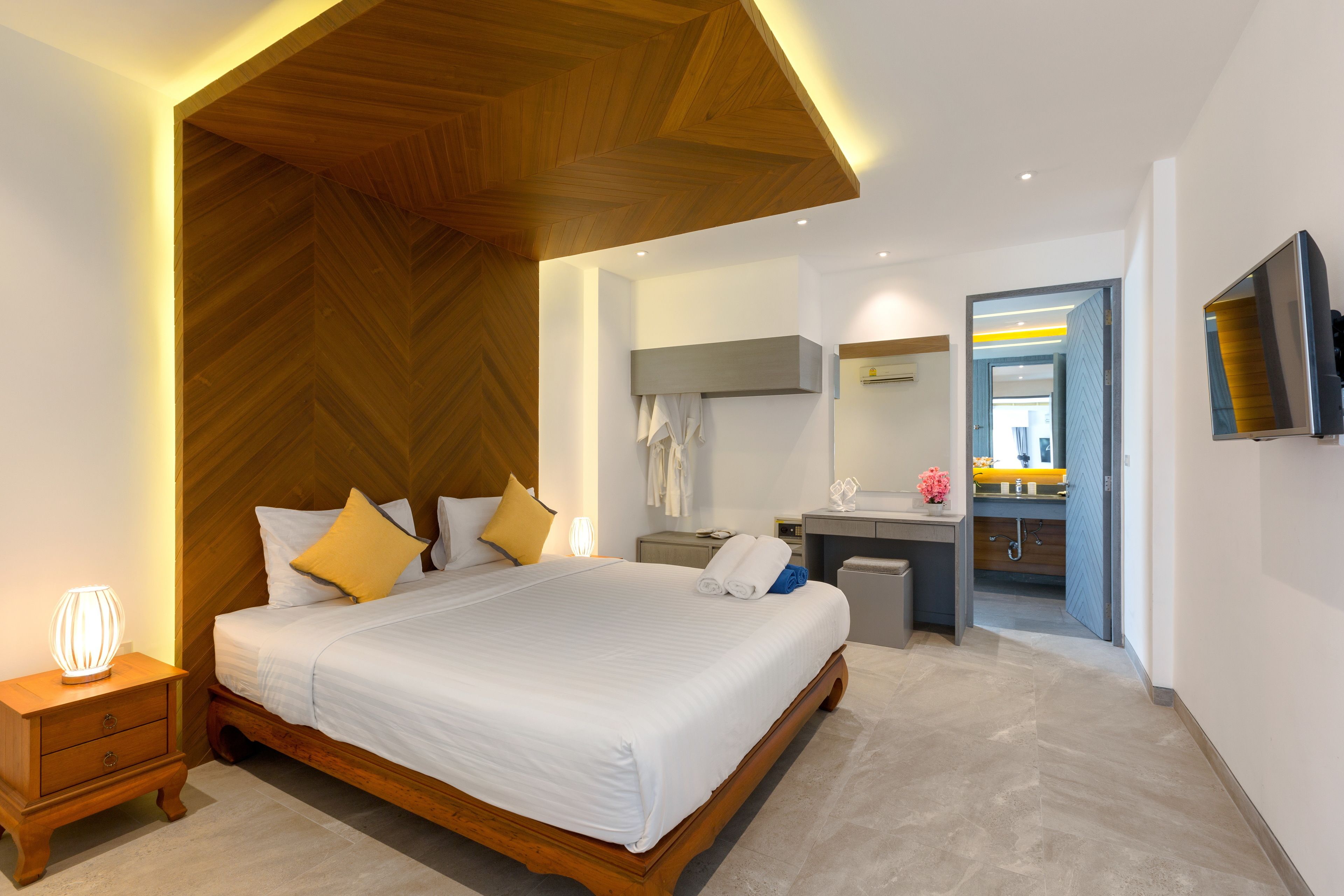 A modern hotel room with a large bed, bedside table, and a desk with a chair.