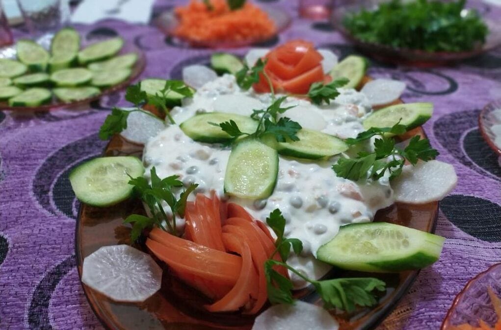 Un plato de comida con pepinos en rodajas, zanahorias y salsa cremosa, adornado con perejil.