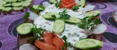 Un plato de comida con pepinos en rodajas, zanahorias y salsa cremosa, adornado con perejil.