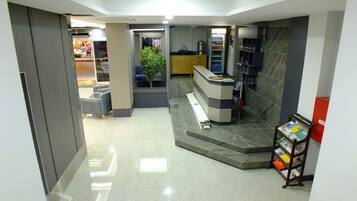 Un área de recepción con mostrador, una planta, máquina expendedora y un atril para revistas.