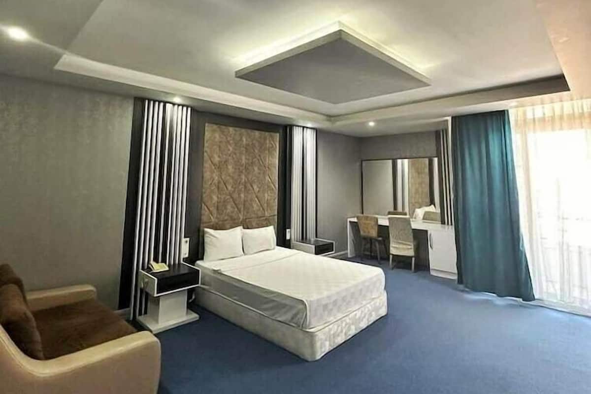 A modern hotel room with a large bed, a desk, a chair, and a sofa.