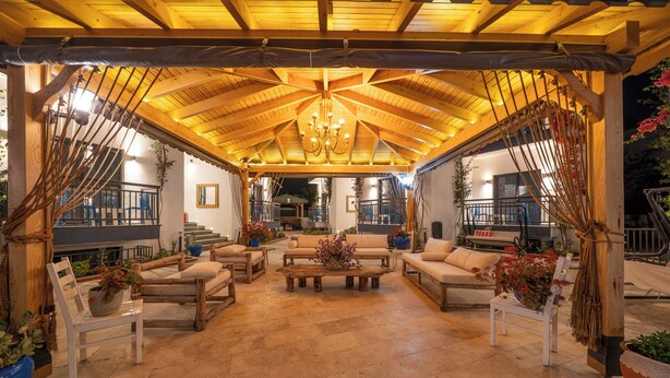 Une terrasse extérieure couverte, aménagée avec des meubles en bois, une table basse centrale et un lustre.