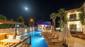 Un espace aménagé au bord de la piscine, avec des chaises longues et des parasols, un mur en pierre et un bâtiment doté de balcons.