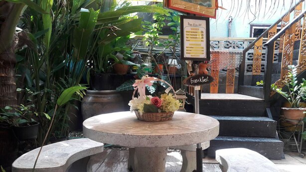 Una mesa de piedra con un cesto de flores, rodeada de plantas en macetas, en un patio con escalones que llevan a una escalera.