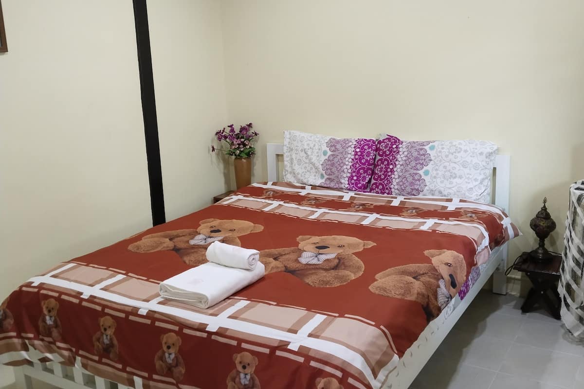 A neatly made bed with a teddy bear themed bedspread, a white headboard, and a small bedside table with a lamp.