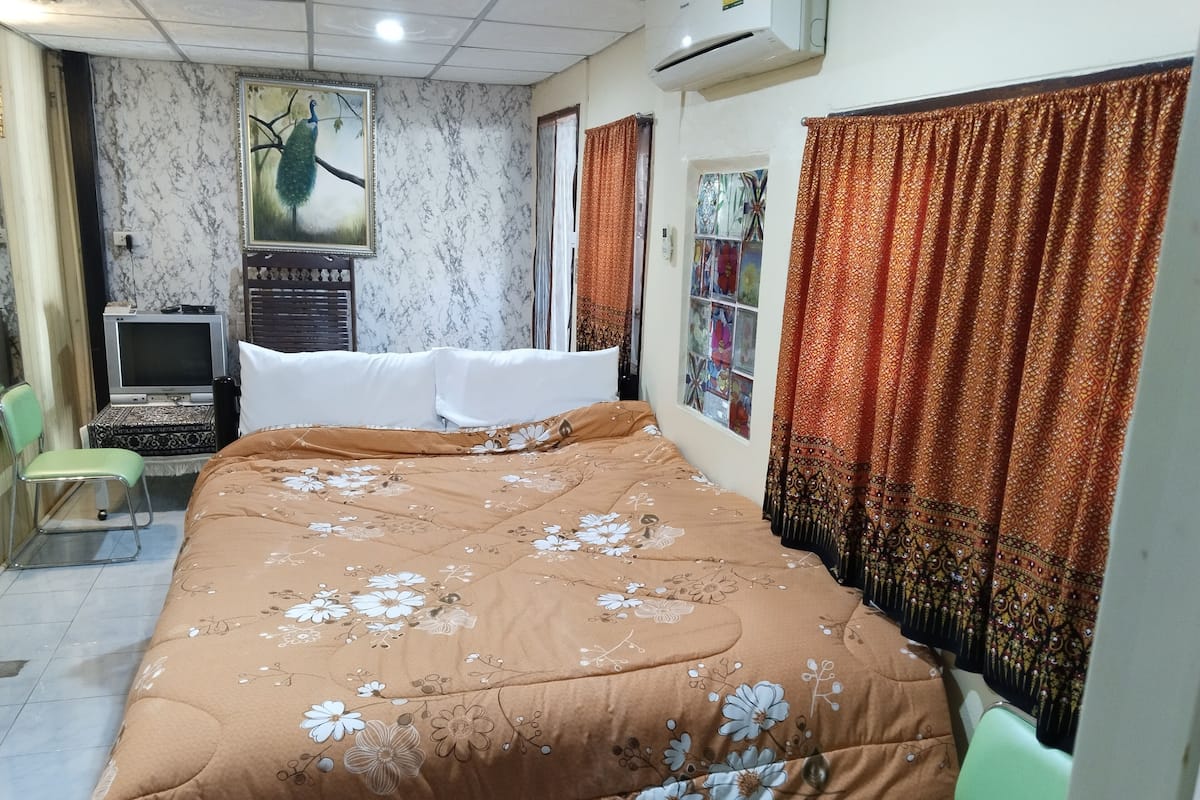 A bedroom with a bed, a television, a chair, and a window with curtains.