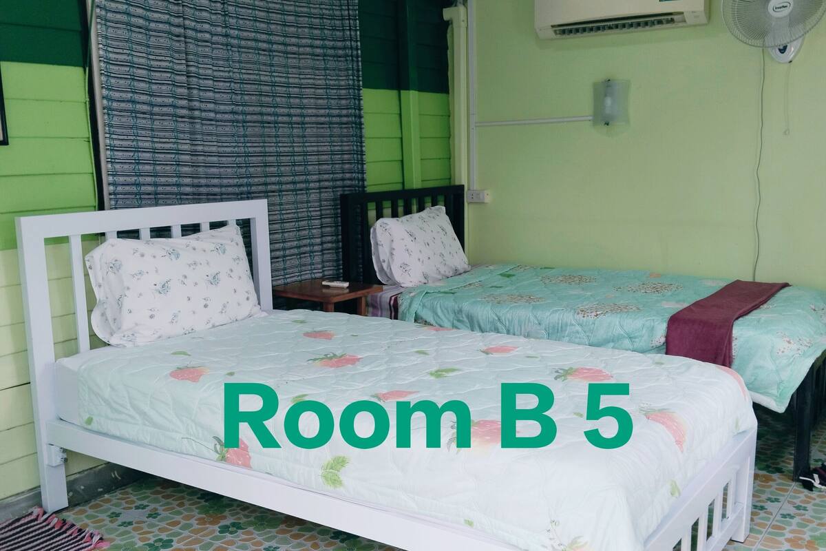 A room with two beds, a window with curtains, an air conditioner, and a fan.