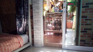 Una habitación con una cama, una ventana con cortina, un muro de ladrillo y una puerta que da a una tienda.
