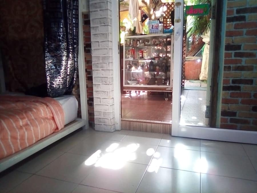 Een kamer met een bed, een raam met gordijn, een bakstenen muur en een deur naar een winkel.