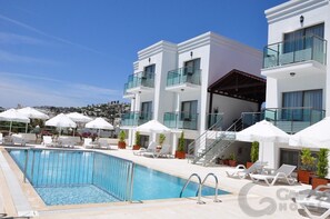 A modern hotel with a swimming pool, sun loungers, and white umbrellas.