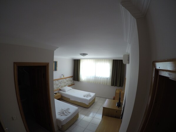 A hotel room with two single beds, a small desk, a mirror, and a window with curtains.