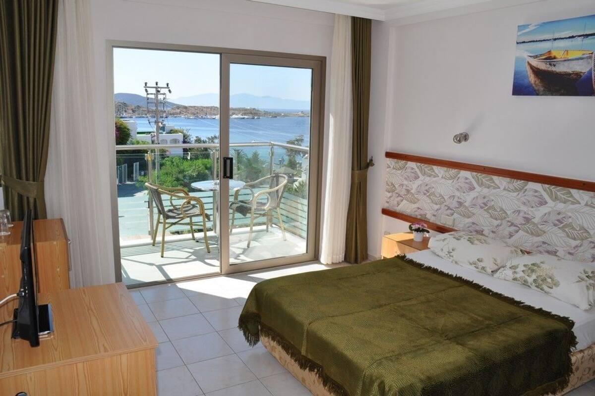 A bedroom with a bed, a wooden desk, a chair, and a balcony with a view of the sea.