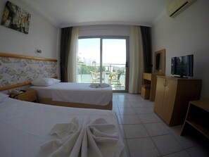 A hotel room with two beds, a TV, a wooden cabinet, and a balcony with outdoor furniture.