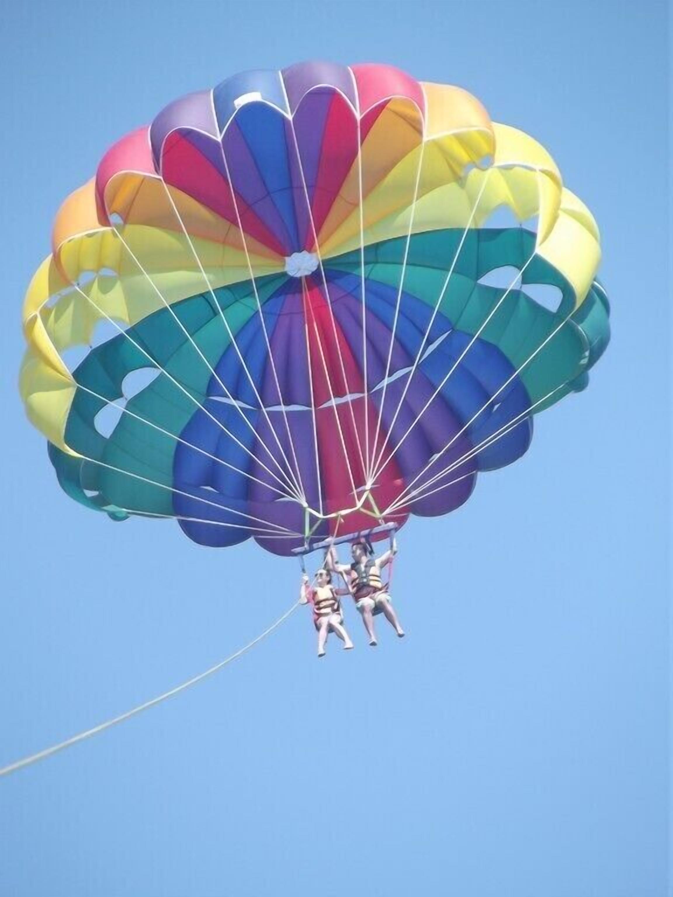 A person parachuting with a multicolored parachute against a clear sky.