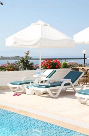 A poolside area with lounge chairs and umbrellas, a clear view of the sea, and a tiled pool.