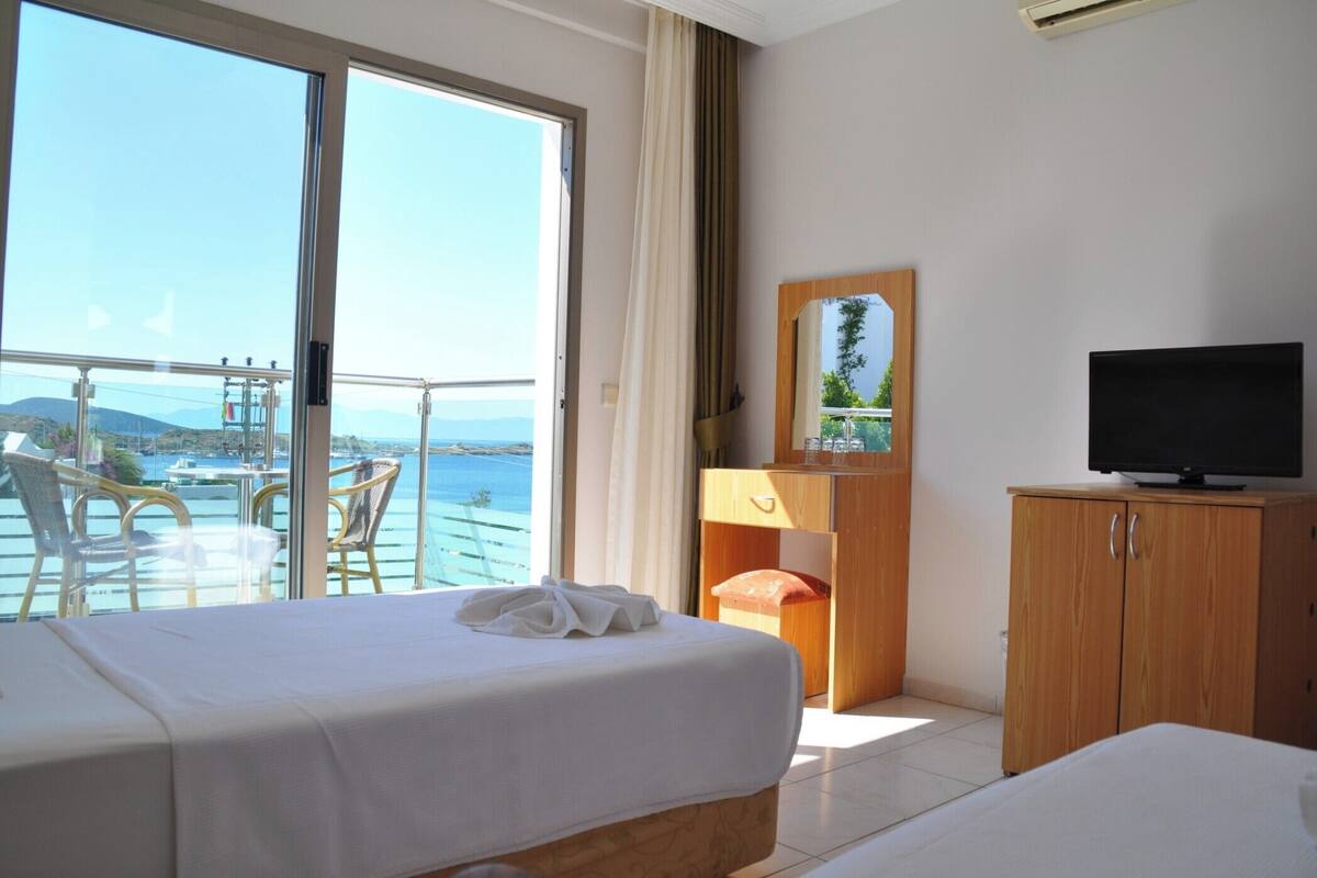 A hotel room with a bed, a television, a wooden cabinet, and a balcony with a view of the sea.