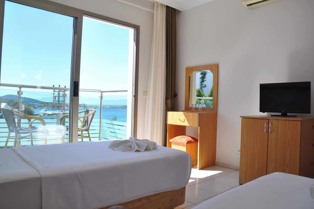 A hotel room with a bed, a television, a wooden cabinet, and a balcony with a view of the sea.