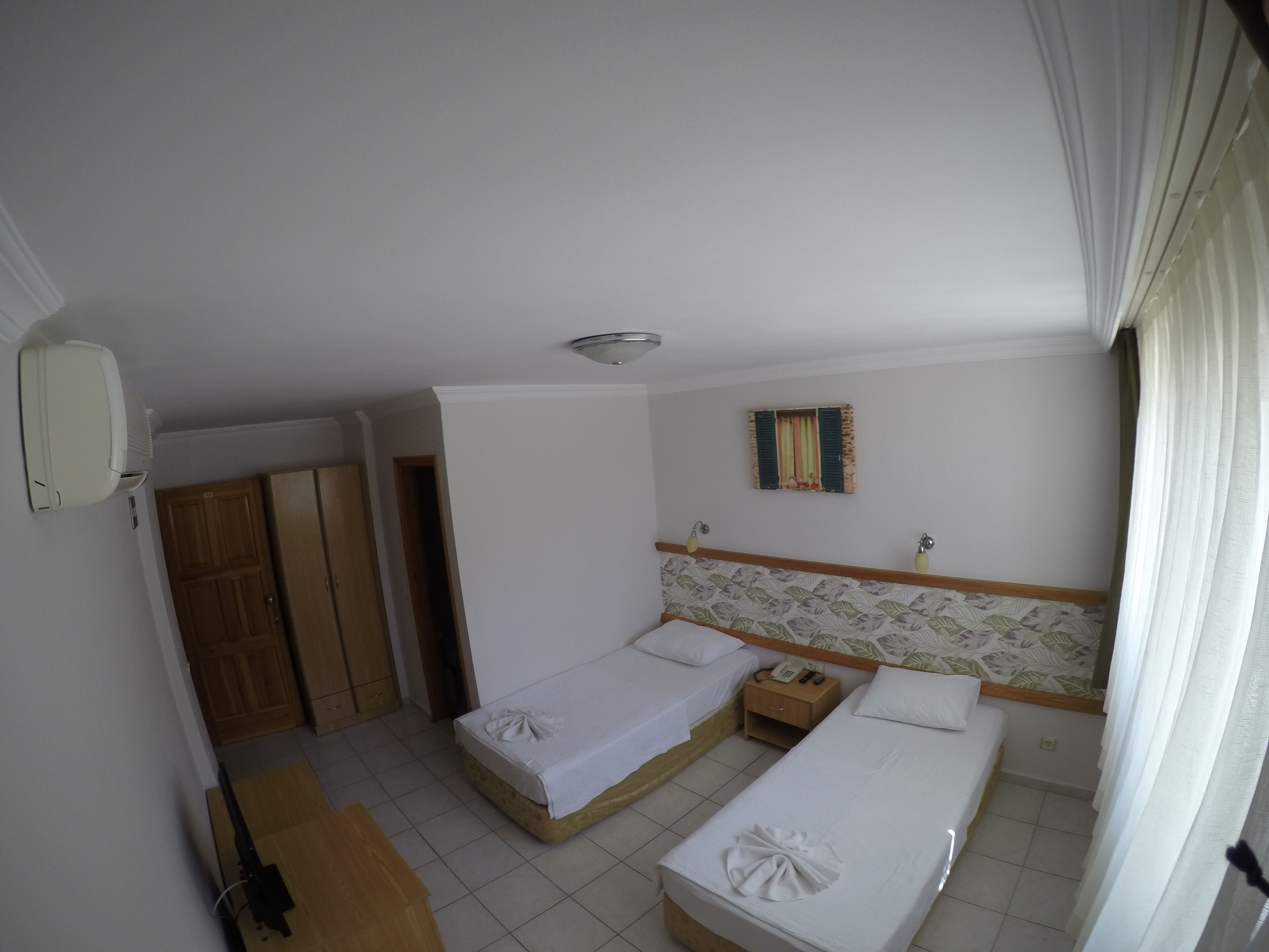 Habitación de hotel con dos camas, un armario de madera, una mesita de noche con teléfono y una ventana con cortinas.