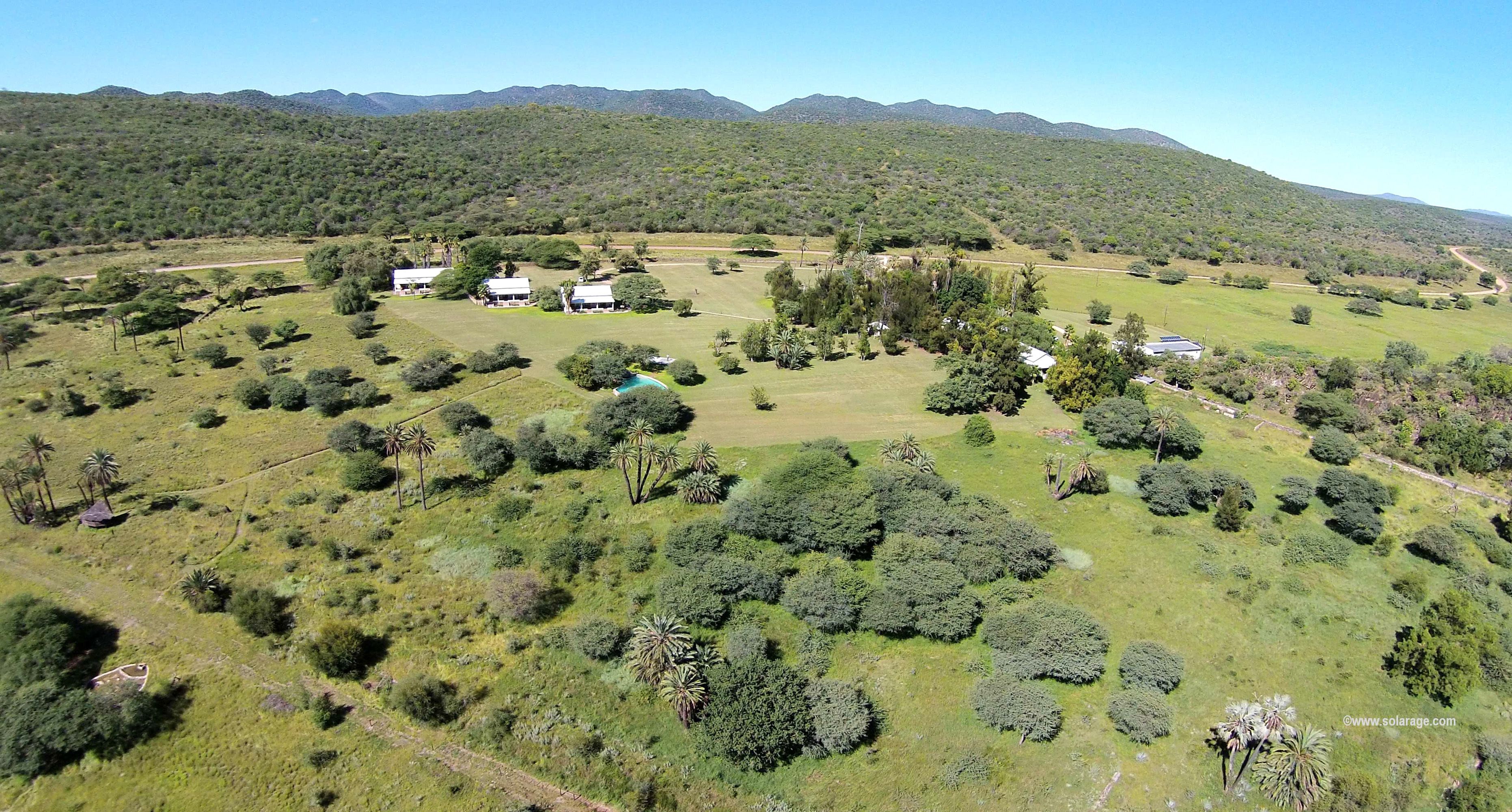 An aerial view of a rural property with multiple buildings, a swimming pool, and surrounding greenery.