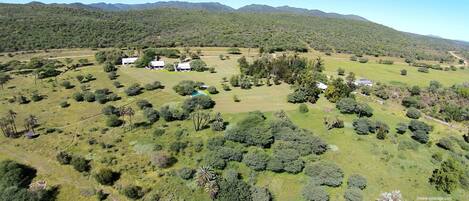 An aerial view of a rural property with multiple buildings, a swimming pool, and surrounding greenery.