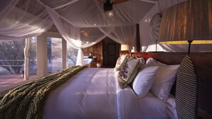 A spacious bedroom with a large bed, a ceiling fan, and a view of the outdoors. - Evolve Back Kalahari (Hainaveld Game Farm)