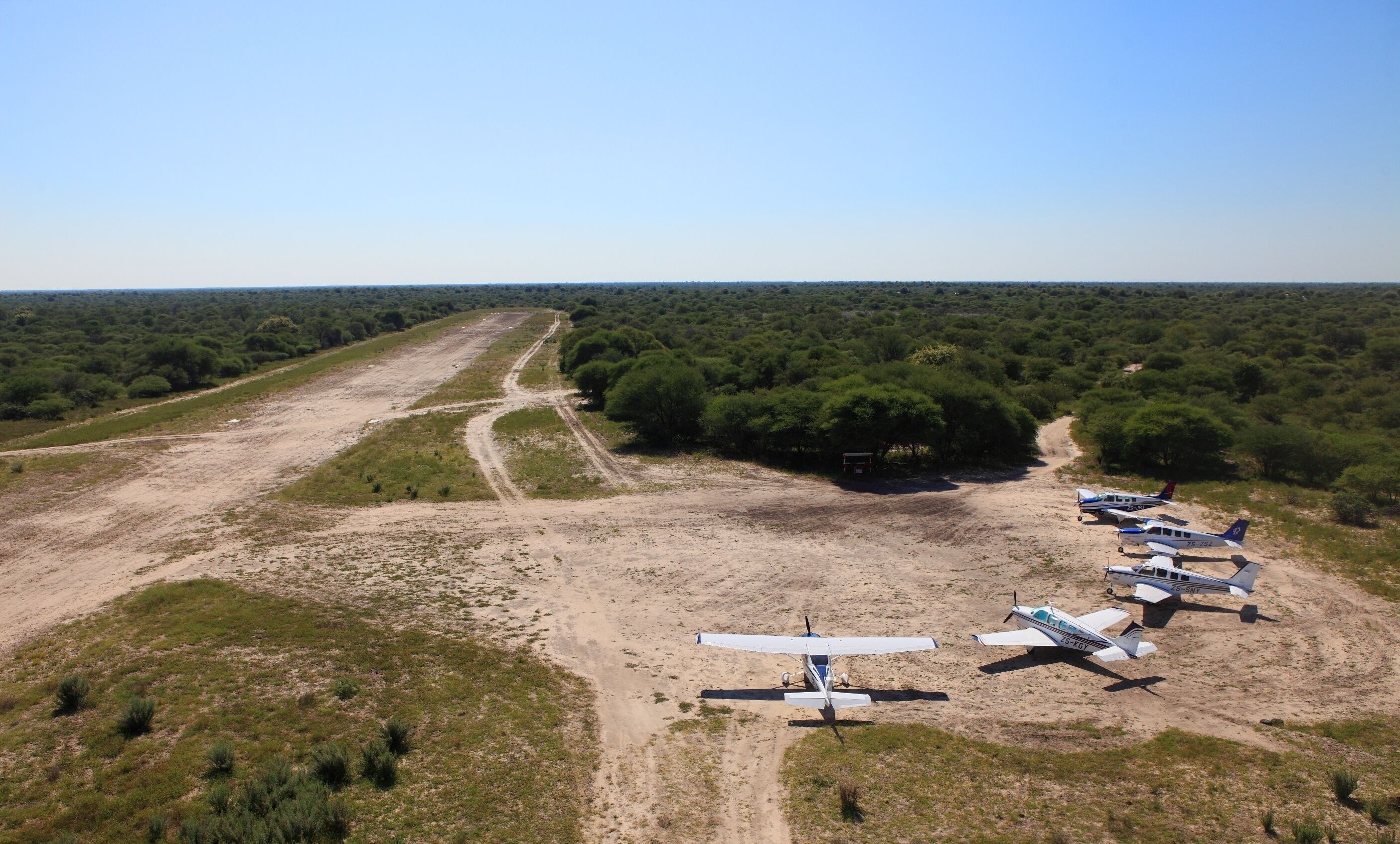 An aerial view of a remote airstrip with several small aircraft parked.