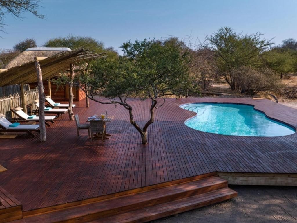 Una terraza de madera con piscina, sillas de descanso y una pequeña mesa.