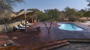 A wooden deck with a swimming pool, lounge chairs, and a table with a drink. - Evolve Back Kalahari (Hainaveld Game Farm)