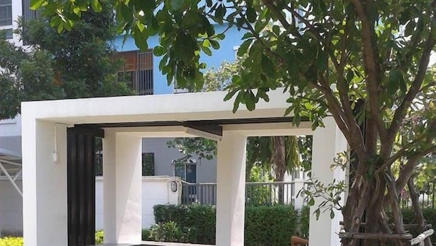 A modern outdoor seating area with a concrete bench and a tree in the foreground. - The Kith Condo Garden View (Lam Luk Ka)