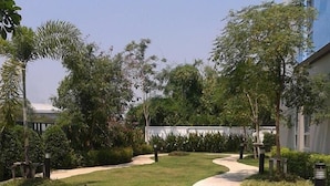 A landscaped garden area with a curved pathway, surrounded by various types of greenery and trees. - The Kith Condo Garden View (Lam Luk Ka)