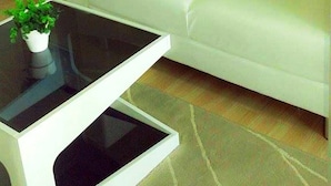 A white sofa with striped cushions and a brown zigzag pillow, a glass coffee table with a plant, and a small white side table. - The Kith Condo Garden View (Lam Luk Ka)