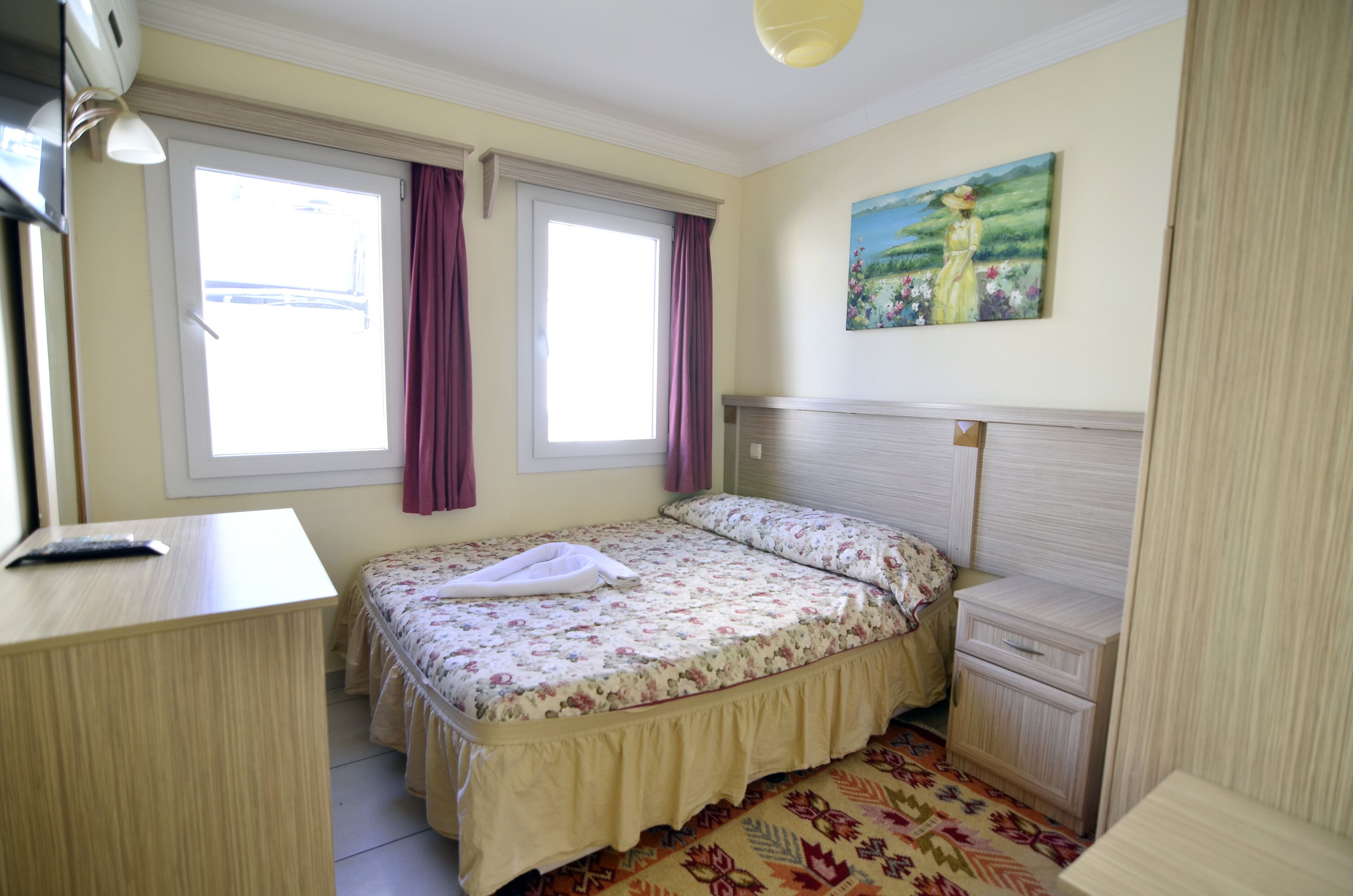 A bedroom with a bed, bedside tables, a desk, and a painting on the wall.