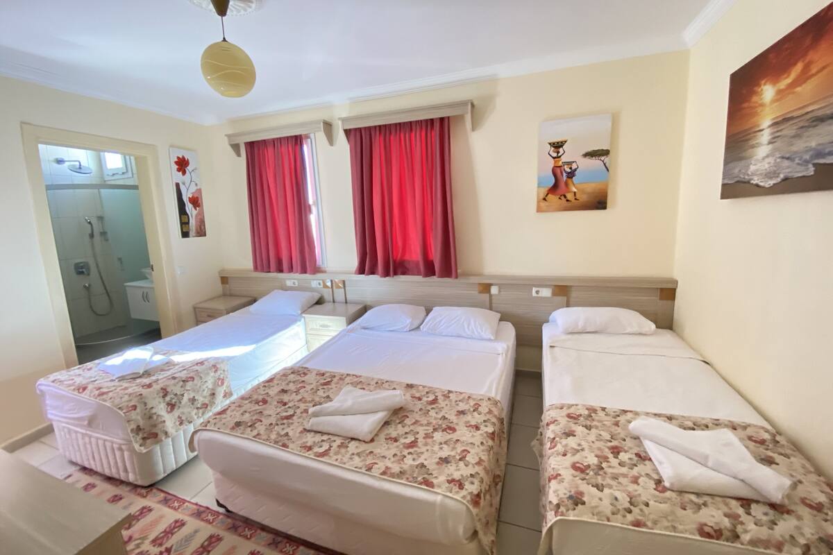 A hotel room with three beds, a shower, and a painting on the wall.