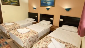 A hotel room with three single beds, each with a floral bedspread and white pillows. There are wall-mounted lamps and a painting above the beds. - Sevin Hotel (Bodrum)