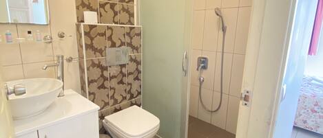 A bathroom with a white sink, toilet, and shower. There is a mirror above the sink and a shower door with a frosted glass panel.