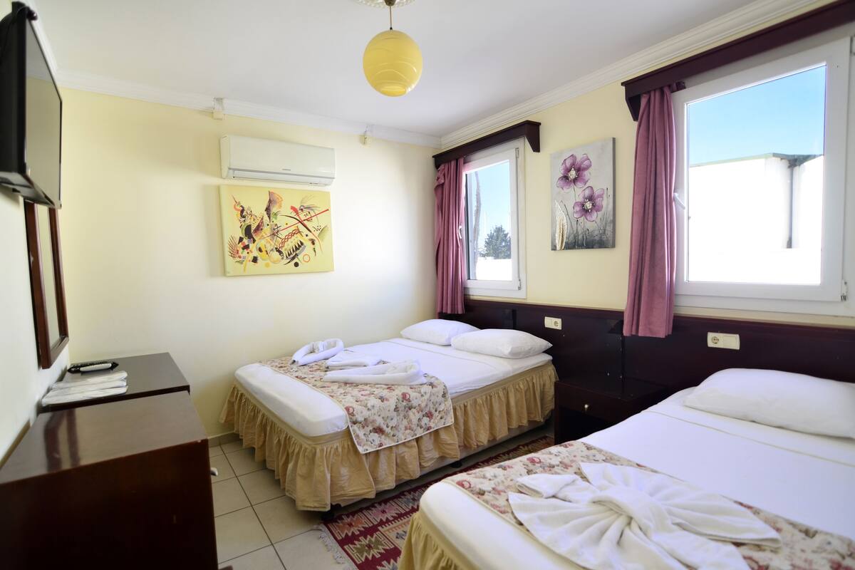 A hotel room with two beds, a desk, an air conditioner, and artwork on the walls.