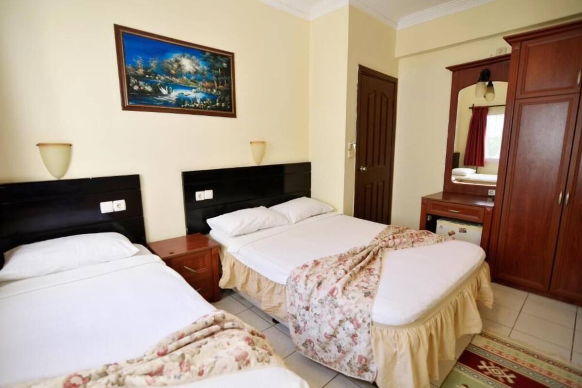 A hotel room with two beds, a painting on the wall, a wooden wardrobe, and a mirror.
