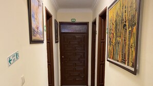 A hallway with a patterned floor, framed artwork on the walls, and a door with a number sign. - Sevin Hotel (Bodrum)