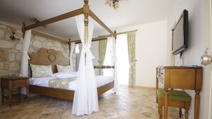 A four-poster bed with a canopy, a wooden nightstand with a telephone, a wooden chair with a green cushion, and a television mounted on the wall. - Alya Ruzgari Otel (Cesme)