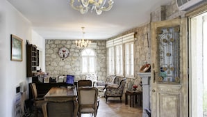 A spacious room with a dining table, chairs, a chandelier, and a stone wall. - Alya Ruzgari Otel (Cesme)