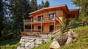 Una cabaña de madera con balcón, cimientos de piedra y rodeada de árboles.