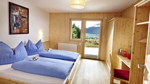 Una habitación con dos camas, un armario de madera, una estantería con libros y vistas al exterior.