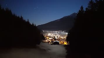 A nighttime view of a town nestled at the base of a mountain, with visible buildings and a snow-covered path leading towards the town.
