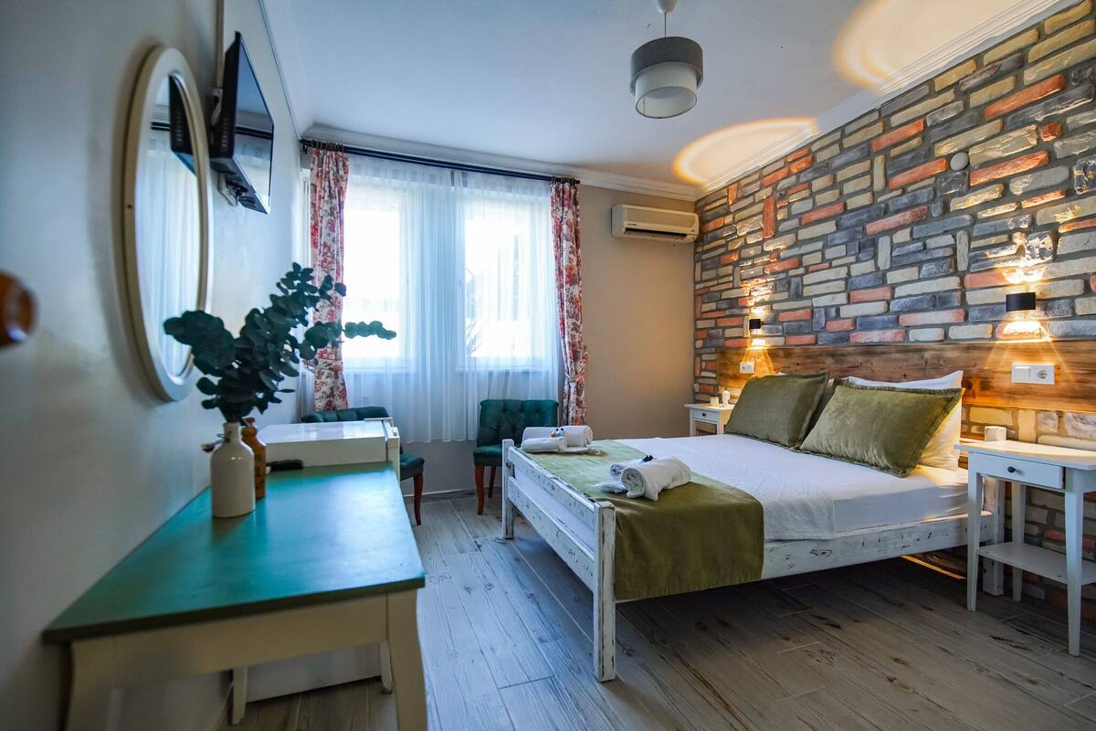 A bedroom with a bed, a desk, a chair, a mirror, and a window with curtains.