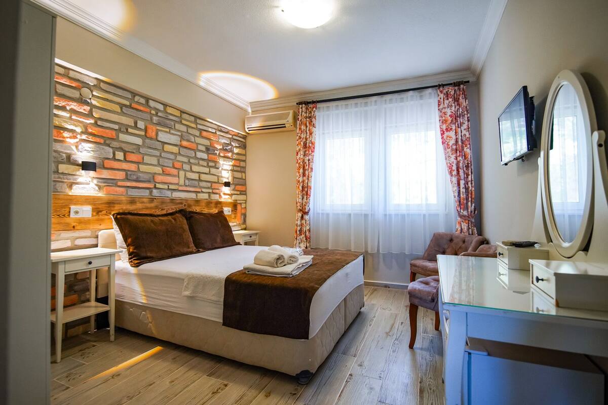 A bedroom with a bed, bedside table, dresser, mirror, and a decorative brick wall.