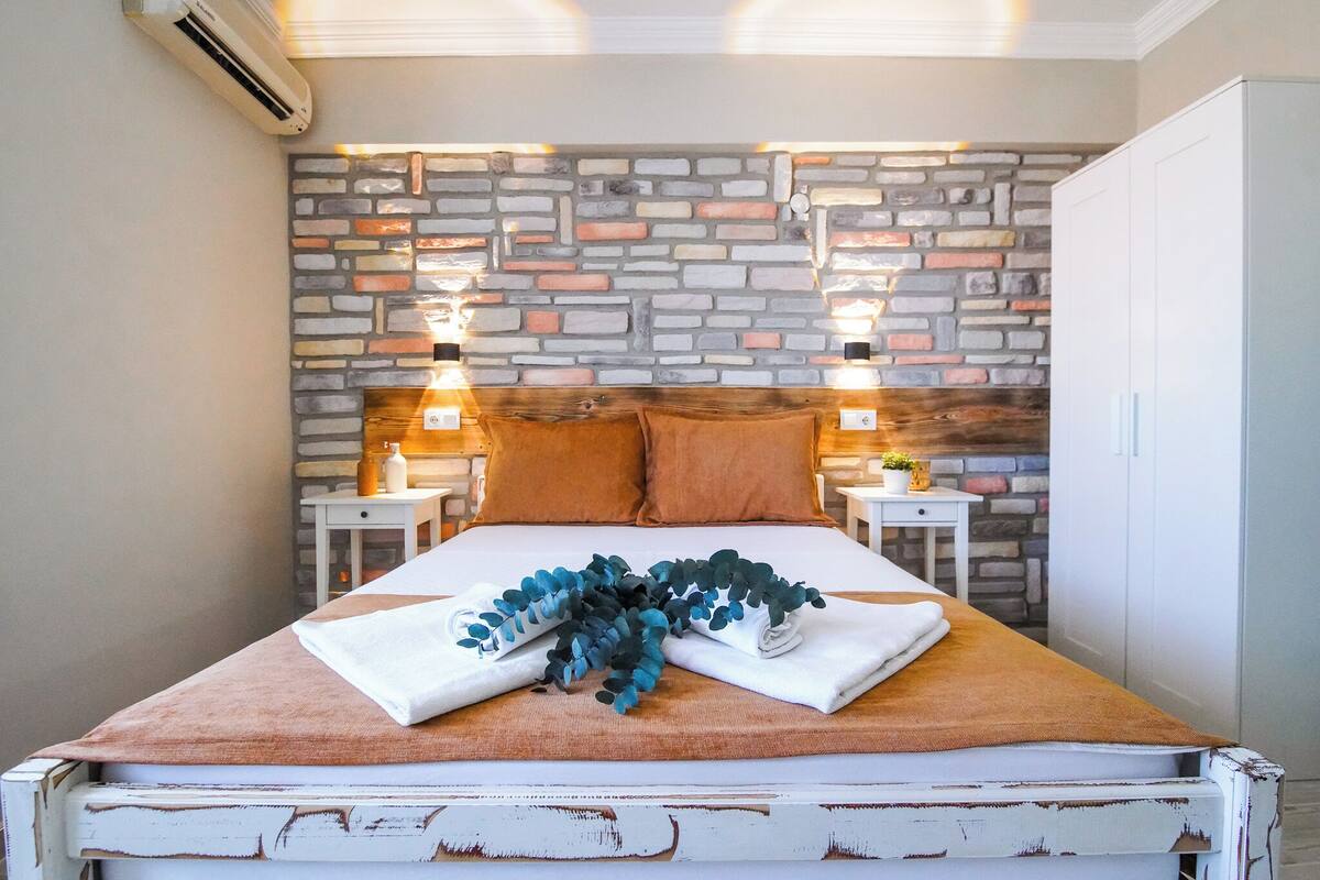 A bed with a stone wall backdrop, two bedside tables with lamps, and a white wardrobe.