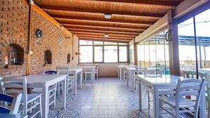 Un patio cubierto con paredes de ladrillo, vigas de madera en el techo y suelo de baldosas. Se disponen mesas y sillas para comer.
