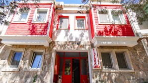 Un edificio de dos pisos con fachada roja y blanca, muros de piedra y una entrada central con puerta roja.